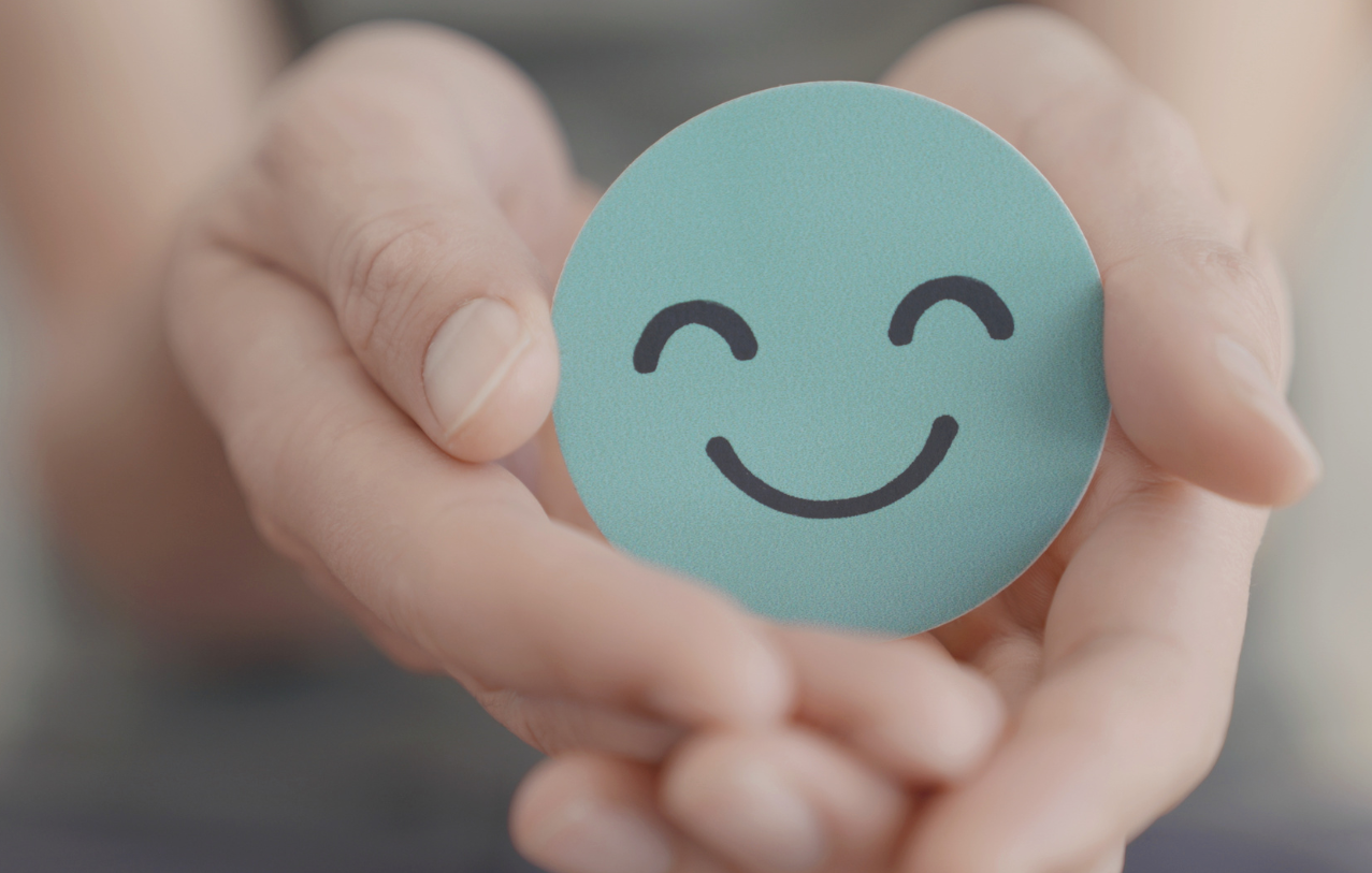 Close up of hands gently holding a blue smiley face icon representing mindfulness therapy and emotional self-care